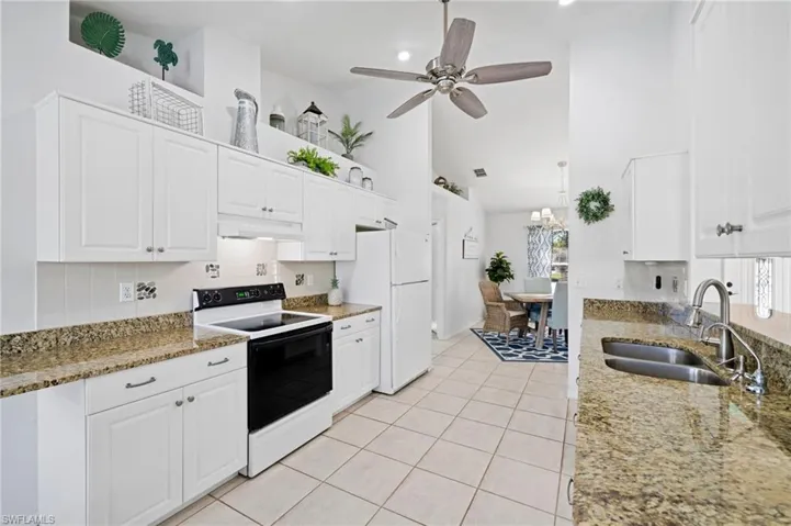 Kitchen with stone counters, sink, white cabinets, and white appliances