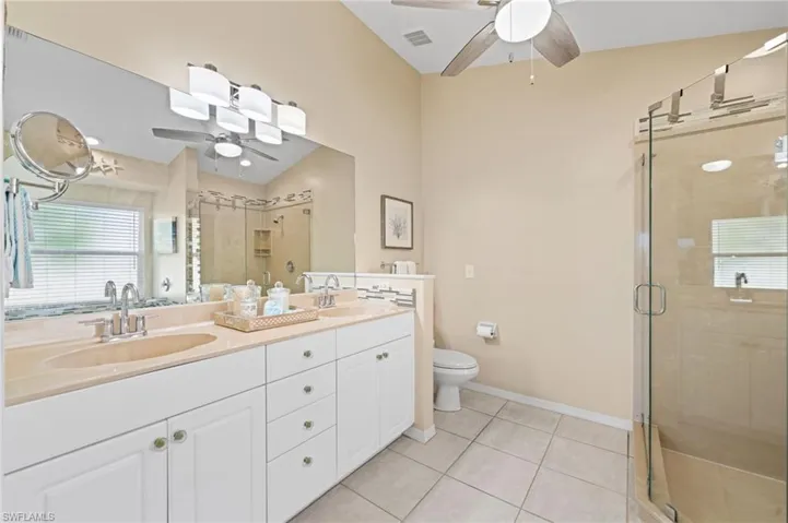 Bathroom featuring tile patterned floors, walk in shower, vanity, ceiling fan, and toilet