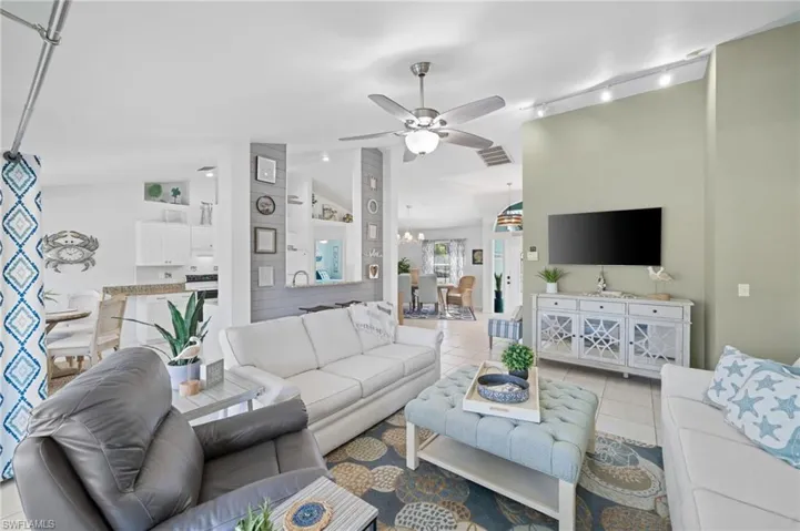 Living room featuring light tile patterned floors, ceiling fan with notable chandelier, track lighting, and lofted ceiling
