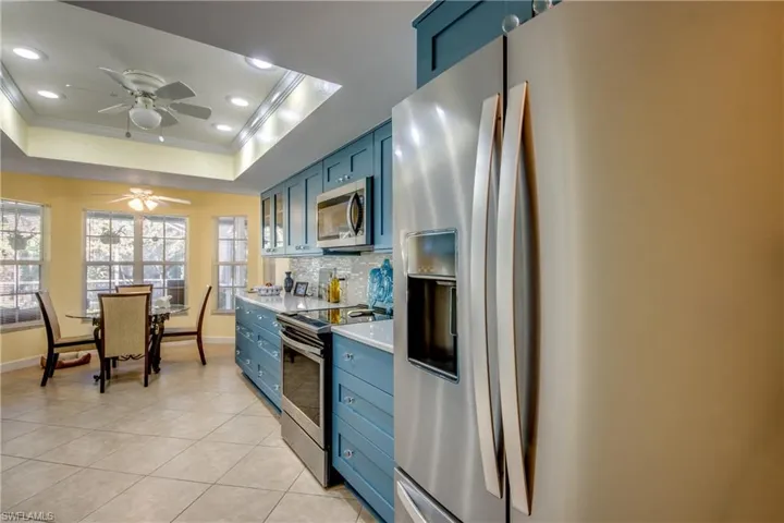 Kitchen with ornamental molding, stainless steel appliances, a tray ceiling, ceiling fan, and blue cabinetry