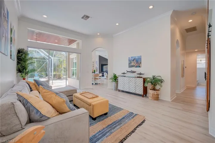 Living room with arched walkways, light wood-style flooring, crown molding, and recessed lighting