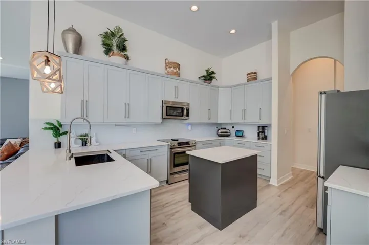 Two tone kitchen with stainless steel appliances, a peninsula, light wood finished floors, a kitchen island, and two tone cabinets