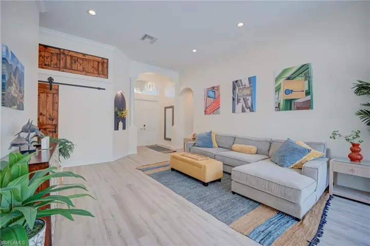 Living area featuring arched walkways, light wood finished floors, recessed lighting, and ornamental molding