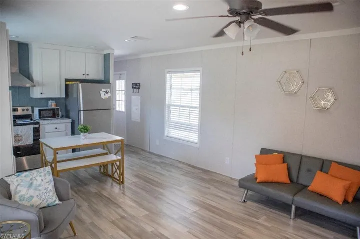 Kitchen featuring crown molding, stainless steel appliances, light wood-type flooring, wall chimney exhaust hood, and a ceiling fan