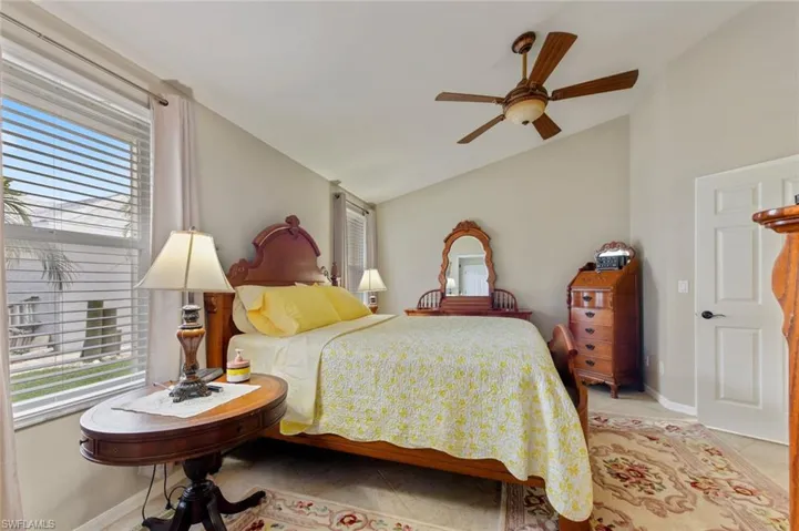 Bedroom featuring vaulted ceiling, multiple windows, light tile patterned floors, and a ceiling fan