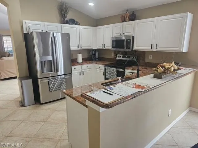 Kitchen with a peninsula, stainless steel appliances, white cabinetry, light tile patterned floors, and dark stone counters