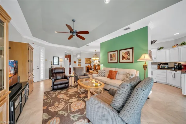 Living room featuring ornamental molding, suspended lighting, ceiling fan, and a tray ceiling
