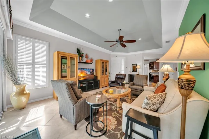 Living room with crown molding, a raised ceiling, recessed lighting, a ceiling fan, and light tile patterned floors