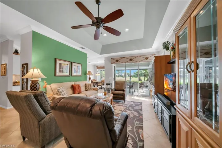 Living room with ceiling fan, light tile patterned flooring, recessed lighting, a raised ceiling, and crown molding