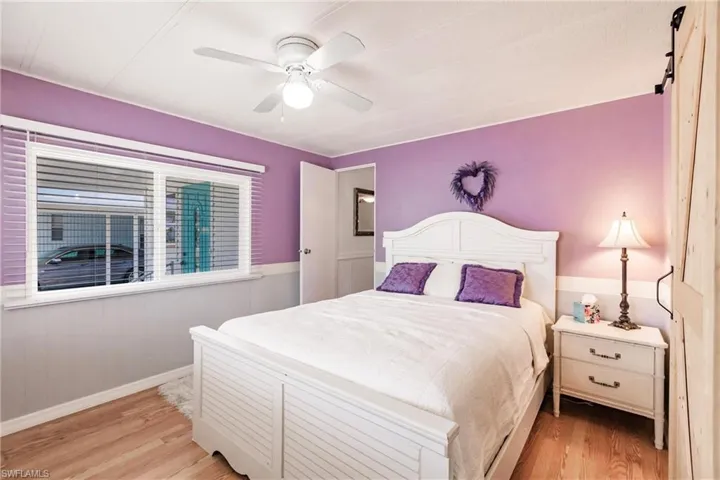 Bedroom featuring a barn door, a ceiling fan, light wood-style floors, baseboards, and wainscoting