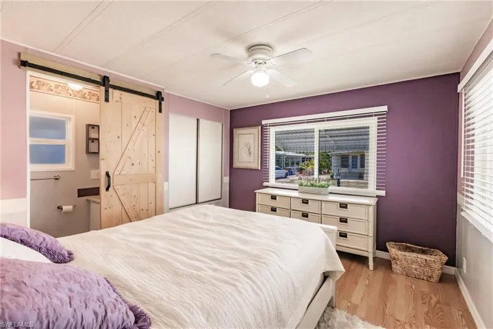 Bedroom with a barn door, light wood-type flooring, a closet, baseboards, and ceiling fan