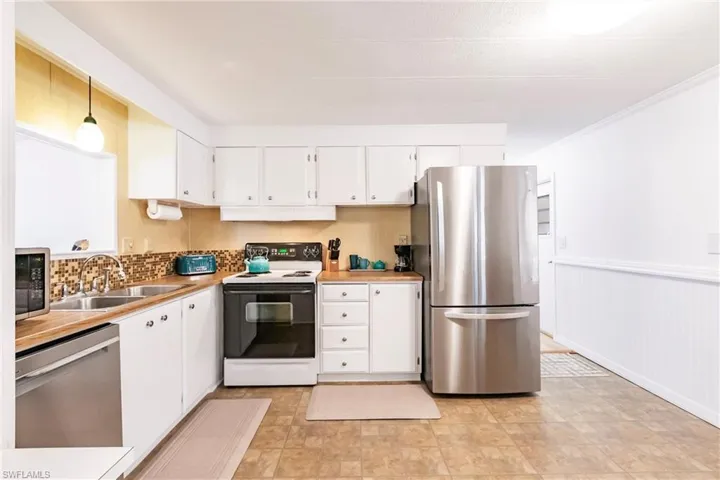 Kitchen with white cabinets, under cabinet range hood, a sink, wainscoting, and appliances with stainless steel finishes