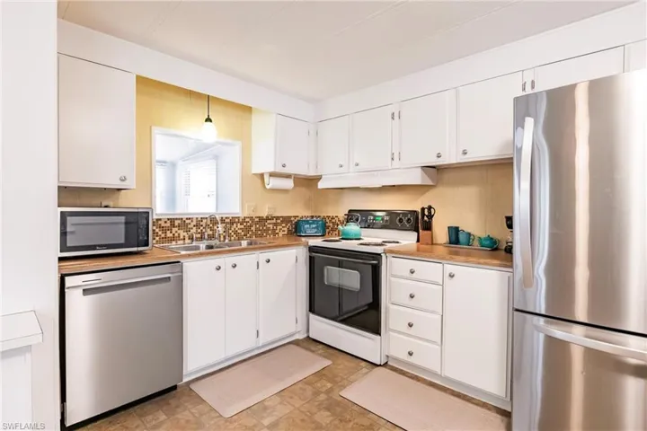 Kitchen featuring white cabinets, stainless steel appliances, a sink, light countertops, and under cabinet range hood