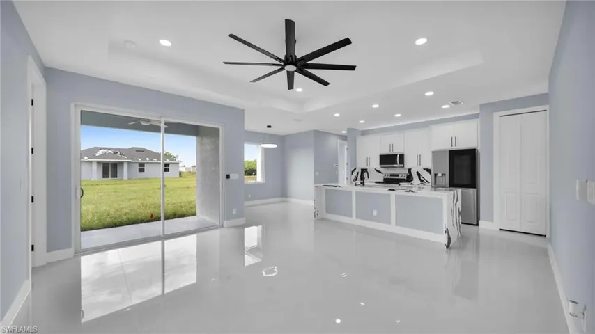 Kitchen with a raised ceiling, recessed lighting, stainless steel appliances, white cabinets, and a ceiling fan