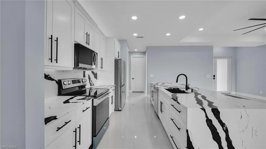 Kitchen with appliances with stainless steel finishes, recessed lighting, white cabinetry, and light stone countertops