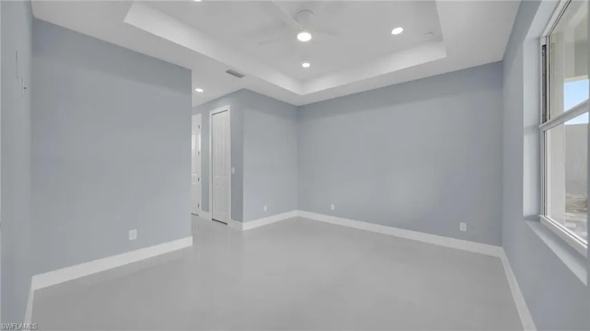 Spare room with healthy amount of natural light, a raised ceiling, ceiling fan, recessed lighting, and finished concrete flooring