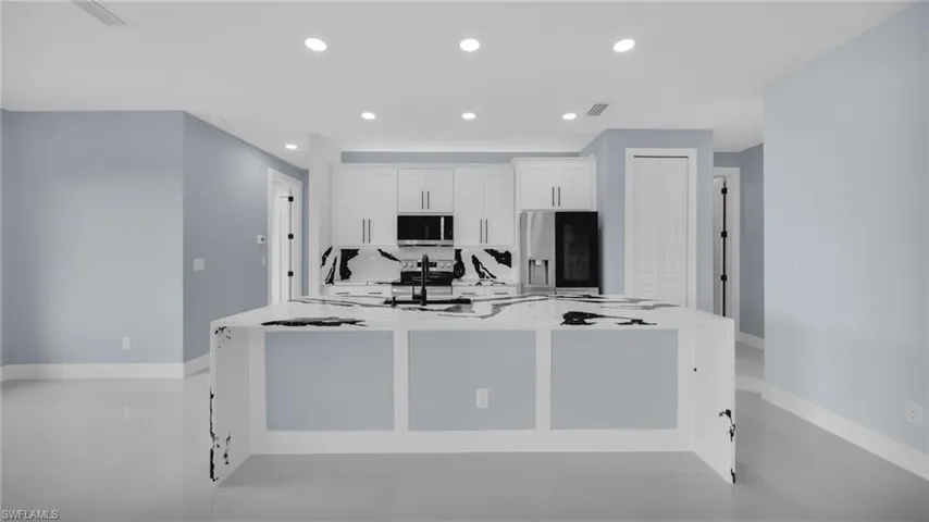 Kitchen featuring refrigerator with ice dispenser, a spacious island, white cabinetry, stainless steel microwave, and recessed lighting