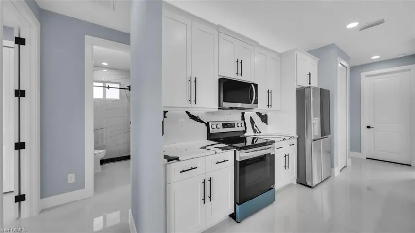 Kitchen featuring appliances with stainless steel finishes, white cabinetry, recessed lighting, light stone counters, and light tile patterned floors