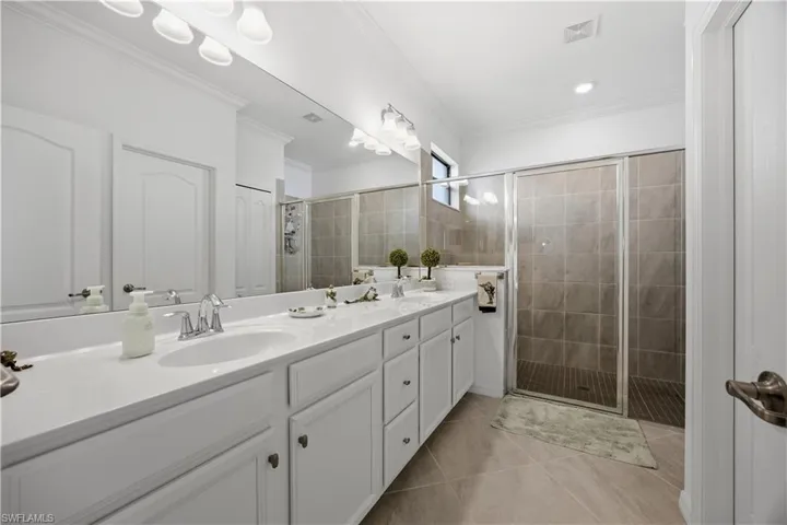 Bathroom featuring a stall shower, double vanity, crown molding, and light tile patterned floors