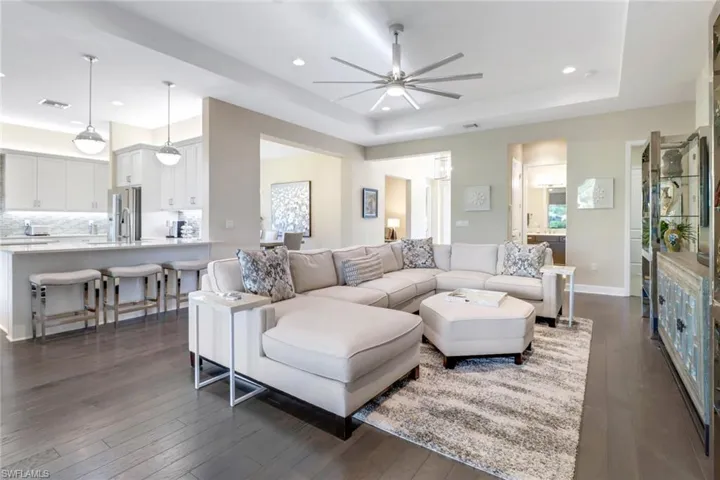 Living room featuring ceiling fan, a raised ceiling, and dark hardwood flooring