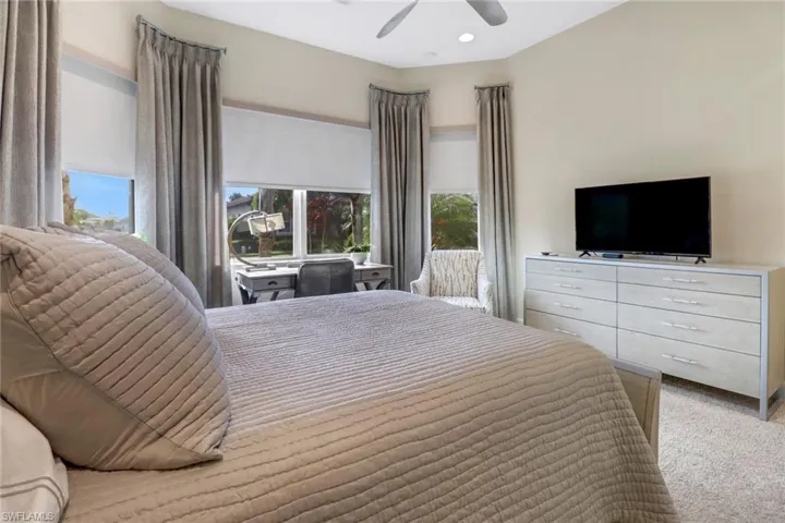 Carpeted bedroom featuring multiple windows and ceiling fan