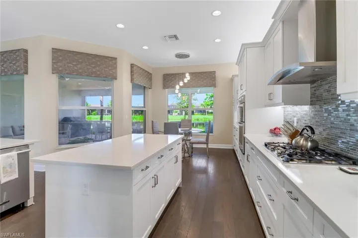 Kitchen with stainless steel appliances, wall chimney range hood, decorative backsplash, white cabinetry, and dark hardwood flooring