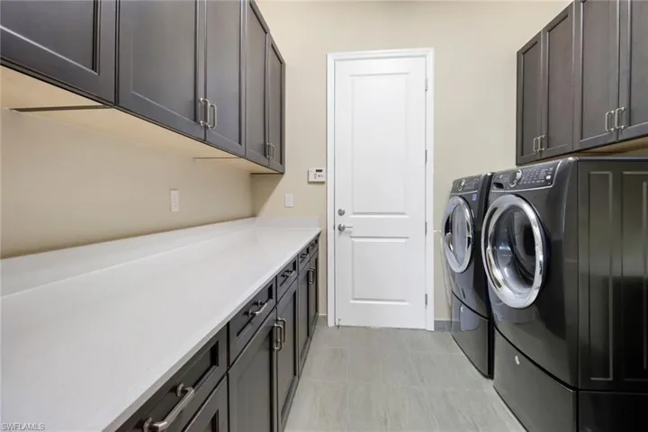 Clothes washing area featuring cabinets, washer and clothes dryer, and light tile patterned floors