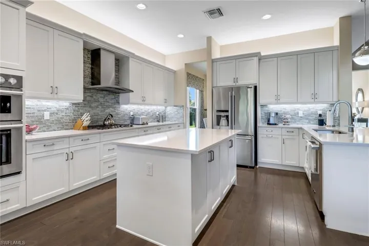 Kitchen featuring wall chimney range hood, backsplash, a center island, dark hardwood flooring, and pendant lighting