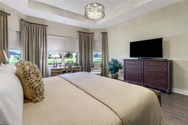 Bedroom with an inviting chandelier, multiple windows, hardwood flooring, and a raised ceiling