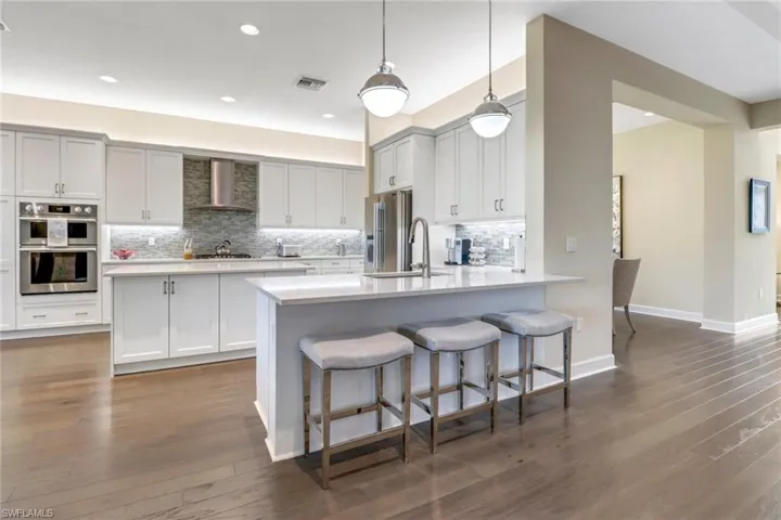 Kitchen with appliances with stainless steel finishes, hanging light fixtures, decorative backsplash, dark hardwood flooring, and wall chimney exhaust hood
