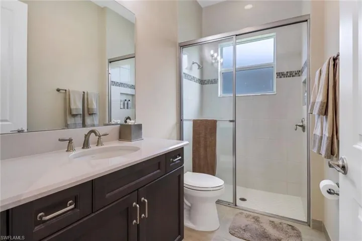 Bathroom featuring a shower with door, vanity, tile flooring, and toilet