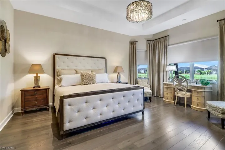 Bedroom with a notable chandelier, multiple windows, hardwood flooring, and a tray ceiling