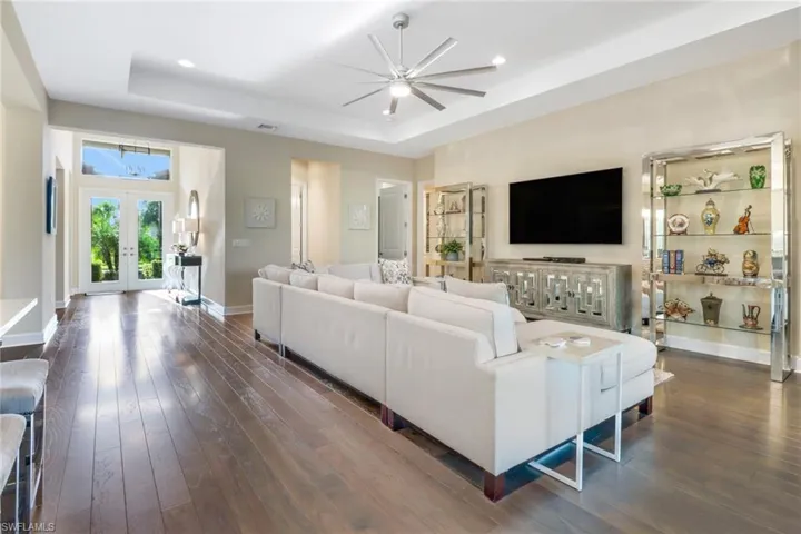 Living room with dark hardwood floors, a raised ceiling, french doors, and ceiling fan