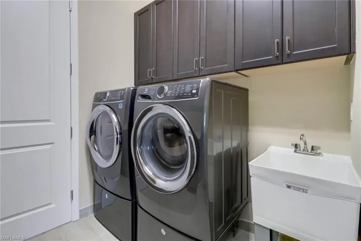 Clothes washing area featuring sink, cabinets, and washing machine and clothes dryer