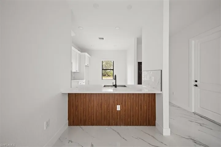 Kitchen with light marble finish flooring, a peninsula, white cabinets, light countertops, and recessed lighting