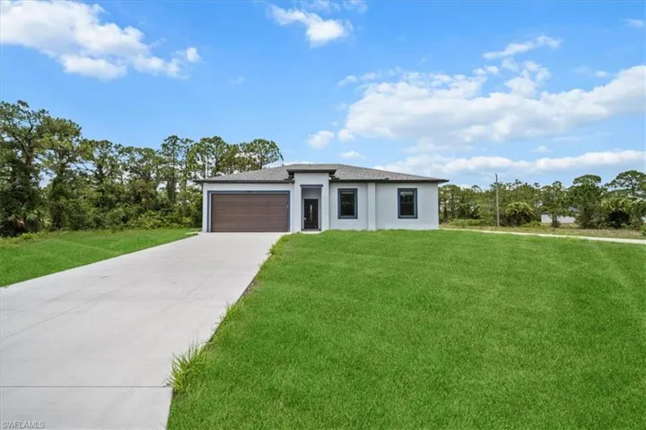 View of front of home with a front yard, a garage, driveway, and stucco siding