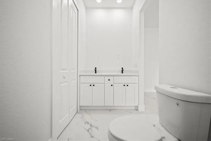 Bathroom featuring marble finish floors, double vanity, and a textured wall