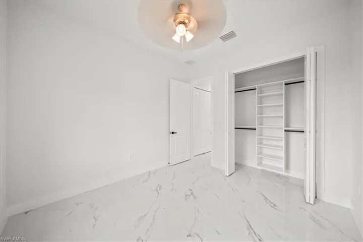 Unfurnished bedroom with marble finish flooring, ceiling fan, and a closet