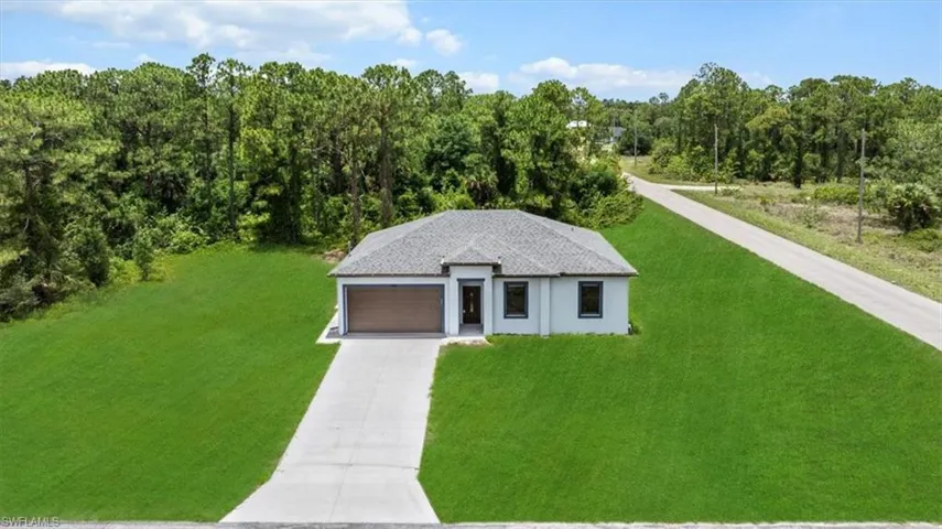View of front of property featuring a front lawn, driveway, a forest view, and an attached garage