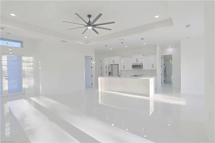 Unfurnished living room with a sink, ceiling fan, a raised ceiling, and recessed lighting