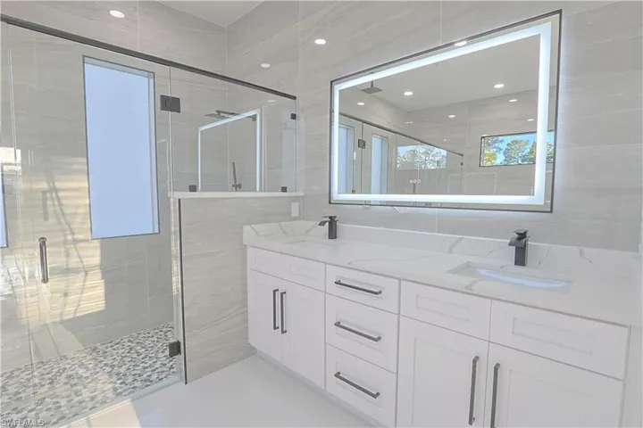 Full bath with a sink, tile walls, a shower stall, and double vanity