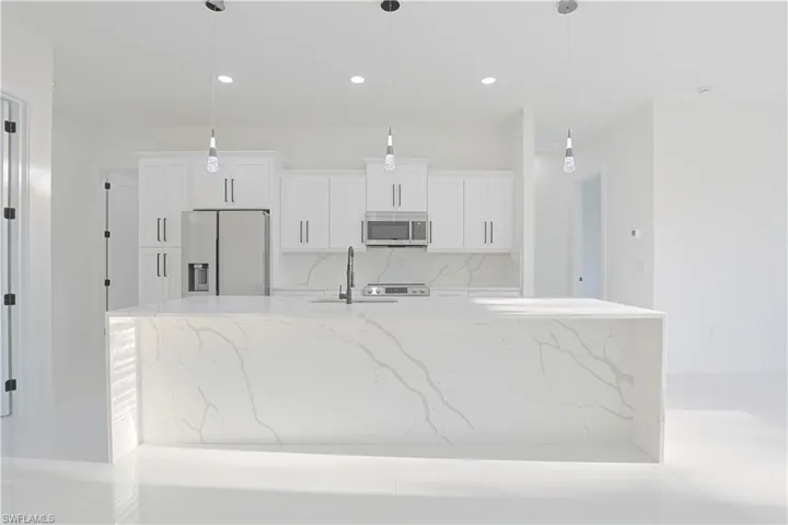 Kitchen with white cabinets, a large island, a sink, appliances with stainless steel finishes, and backsplash