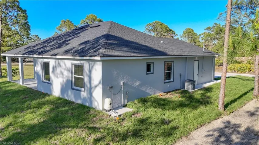 Rear view of house featuring cooling unit, a yard, a shingled roof, and stucco siding