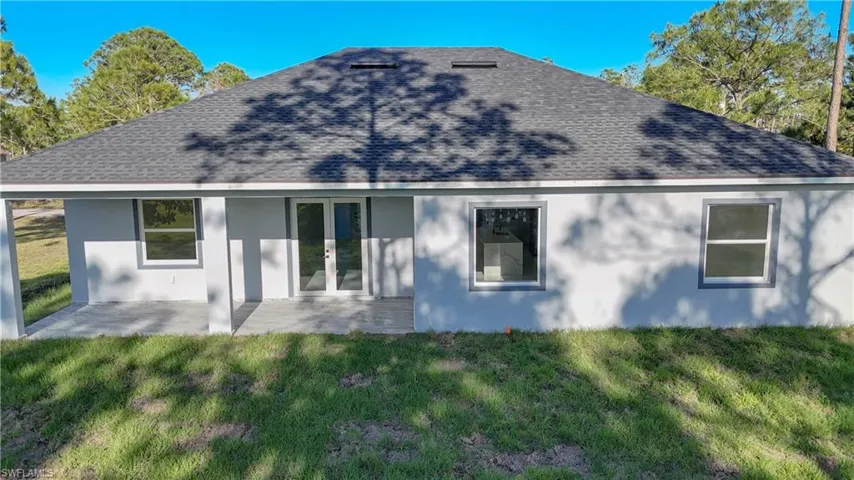 Rear view of house with a yard, a patio, stucco siding, and a shingled roof