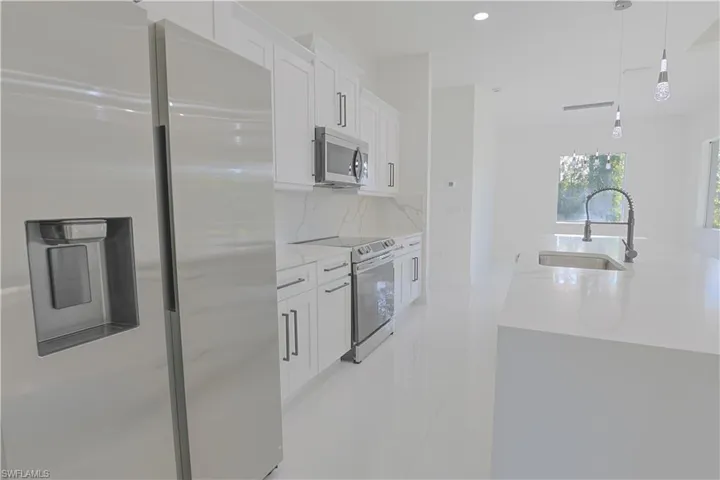 Kitchen featuring white cabinets, a sink, stainless steel appliances, backsplash, and light stone counters
