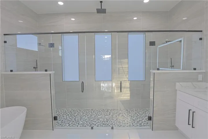 Bathroom with a shower stall, a freestanding tub, vanity, recessed lighting, and tile walls