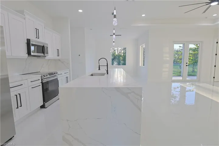 Kitchen with tasteful backsplash, a sink, appliances with stainless steel finishes, recessed lighting, and a center island with sink