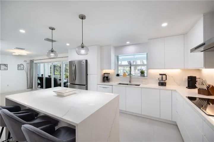 Kitchen featuring freestanding refrigerator, wall chimney exhaust hood, modern cabinets, recessed lighting, and a kitchen island