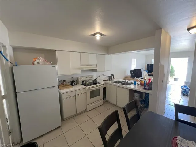 Kitchen with white cabinetry, sink, light tile patterned floors, and white appliances
