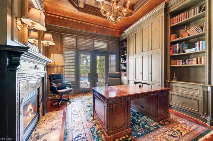 Home office featuring built in shelves, crown molding, dark wood-style floors, a high end fireplace, and hanging lights